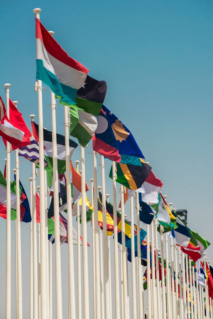 Menus A variety of international flags waving on flagpoles under a clear blue sky.
