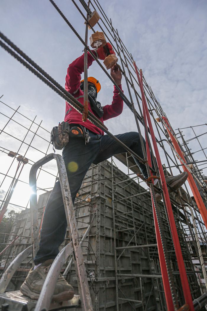 About A construction worker wearing safety gear climbs a steel frame at an outdoor construction site.